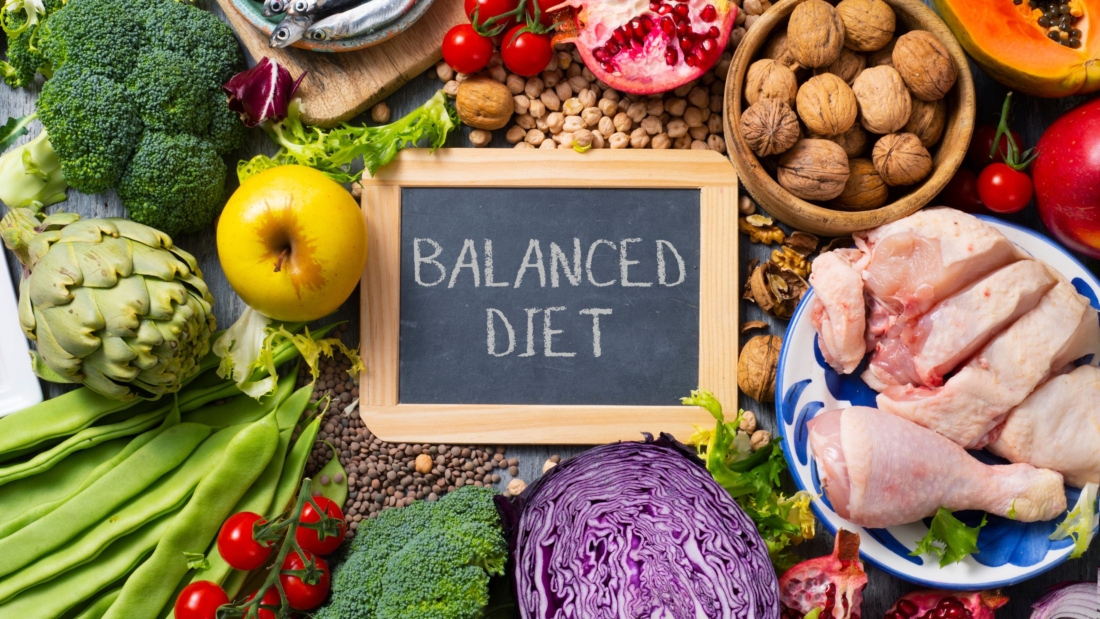 Fresh vegetables, fruit, nuts and chicken around a Balanced Diet chalkboard