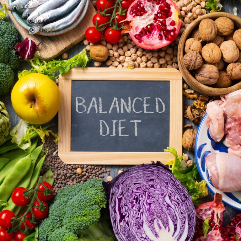 Fresh vegetables, fruit, nuts and chicken around a Balanced Diet chalkboard